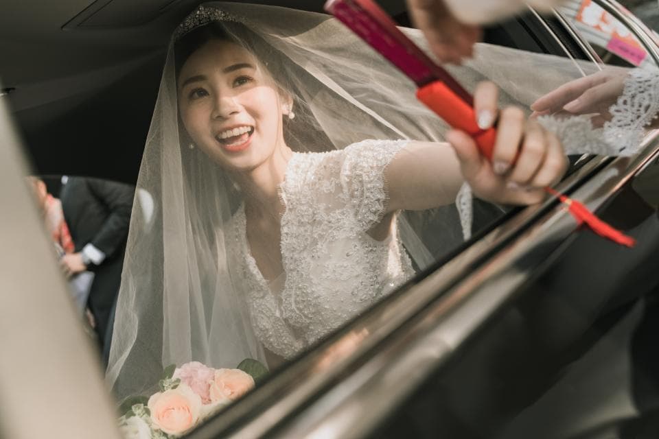 這張照片是一名穿著婚紗的新娘在車窗裡,她正舉著紅色禮金,露出幸福的笑容。