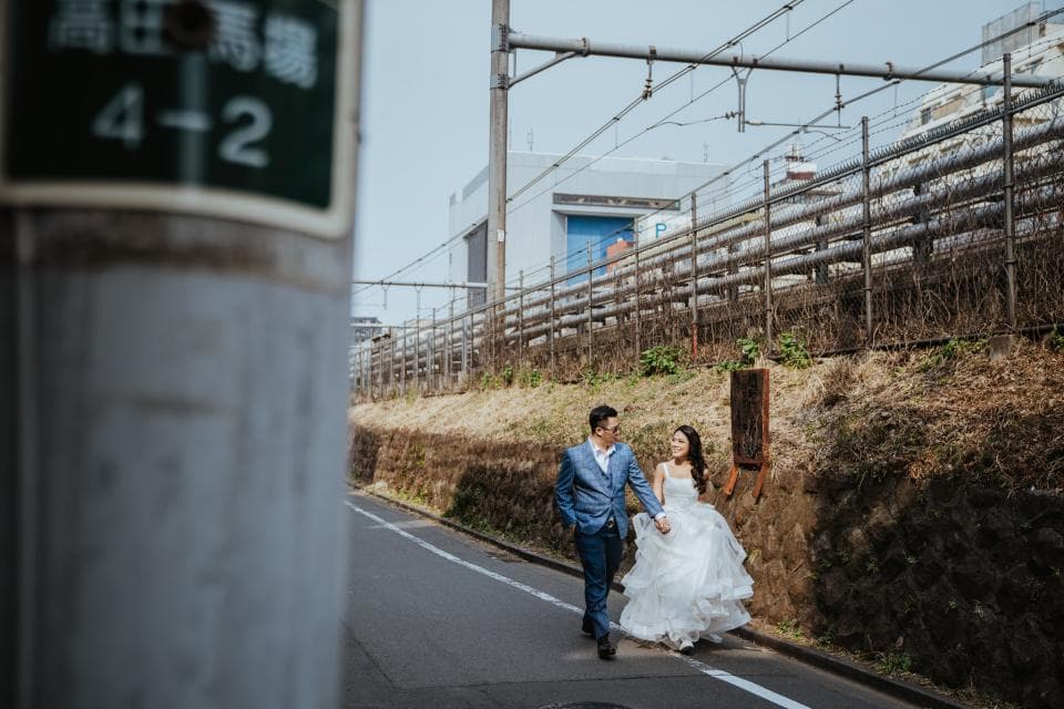 這張照片是一對新人正在道路上漫步,新郎穿著藍色西裝,新娘穿著白色婚紗,他們手牽手,臉上洋溢著幸福的笑容。