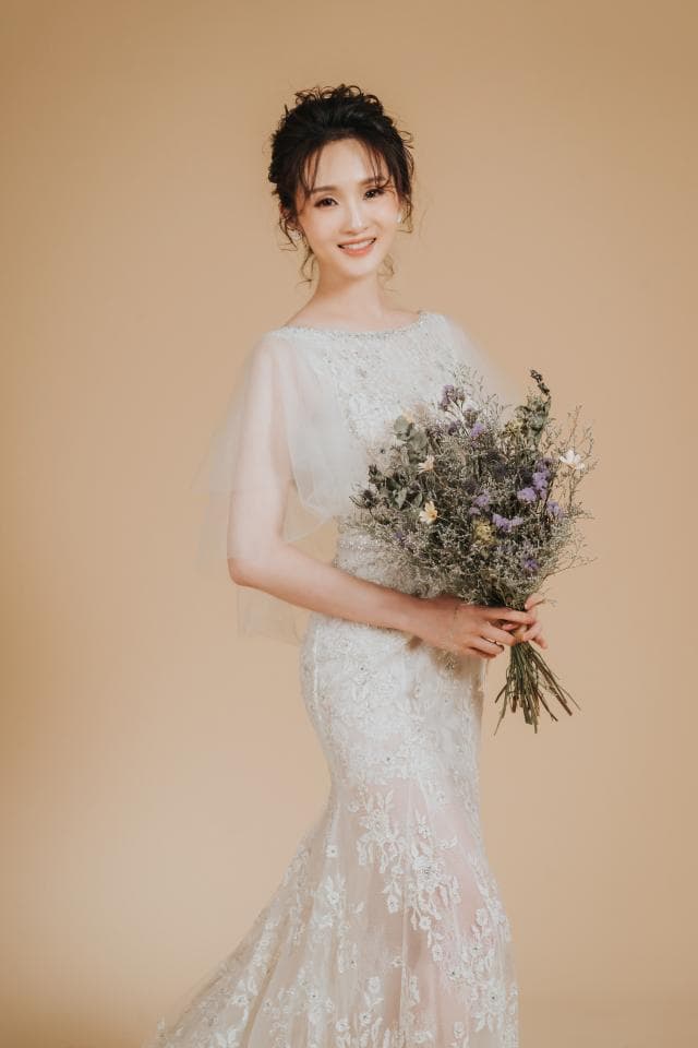這張「婚紗照」的照片是一個穿著白色蕾絲婚紗的新娘,她手持一束乾燥花,並露出幸福的笑容。