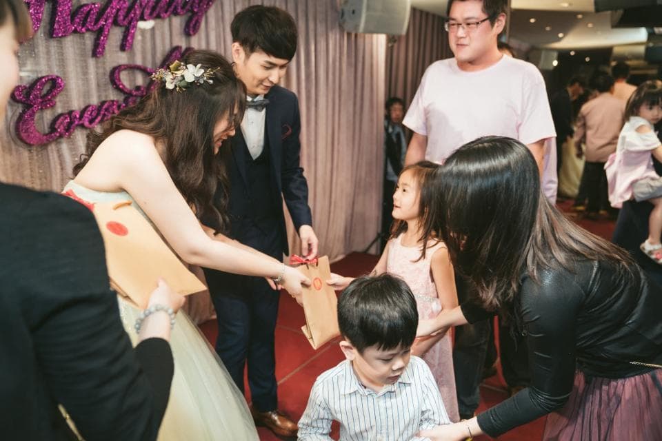 這張婚禮的照片是一對新人正在和親朋好友交換禮物,新郎穿著西裝,新娘穿著白色婚紗,他們看起來很開心。