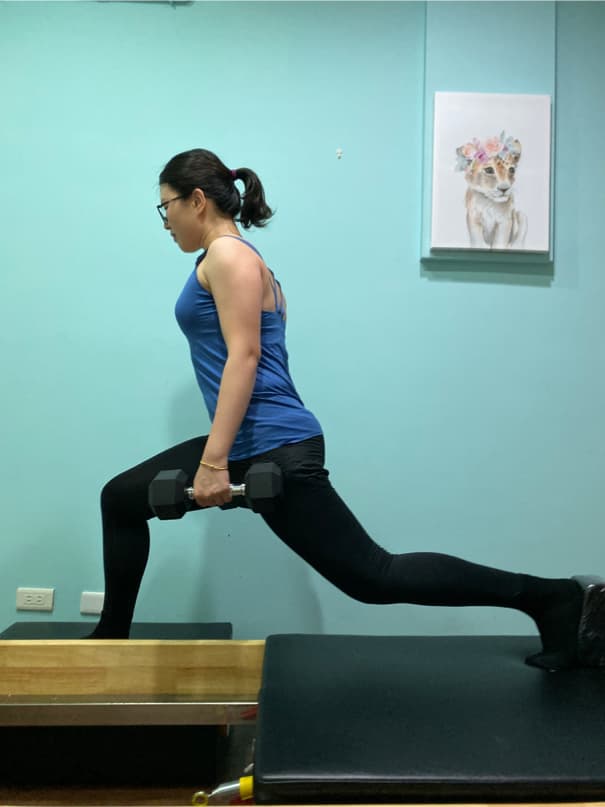 這張照片是一位女性正在做單腿深蹲,她雙手握著啞鈴,左腿伸直,右腿彎曲,右腿著地。