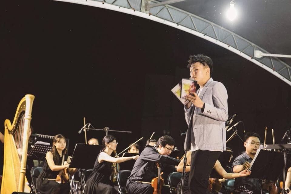 這張照片是一個音樂會,最重要的是站在舞臺中央的男歌手,他手持獎狀,看起來很開心。