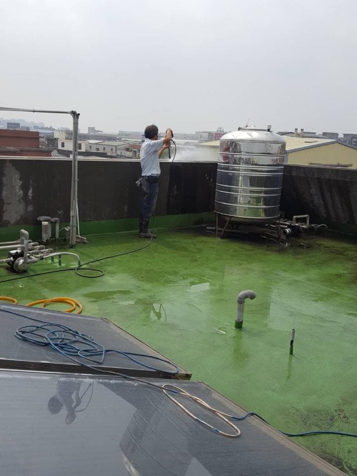 這張照片是一個屋頂,上面有一個大型水塔,以及正在清洗屋頂的工人。