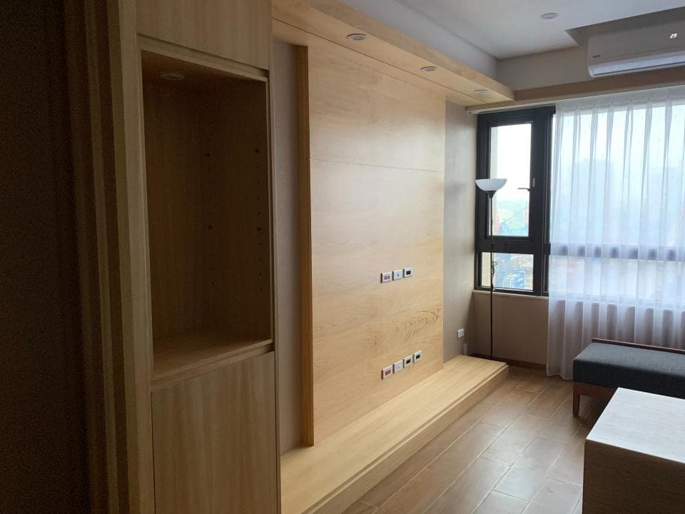 這張照片是一間房間的牆壁,牆壁上有一個木櫃,櫃子有兩個層架,上面放着一些裝飾品。櫃子下方是一個木質的平台,平台上有一個插座。牆壁上還有兩盞燈,可以照亮房間。