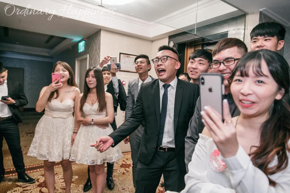 這張照片是 一群人在室內聚會,一個女孩拿著手機自拍,其他的朋友們則圍繞在她身邊,畫面充滿歡樂的氣氛。