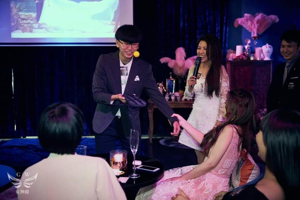 這張照片是一場魔術表演,其中一位魔術師正在表演魔術,他手上拿著一個黑色的道具,看起來像是卡片或其他魔術道具。