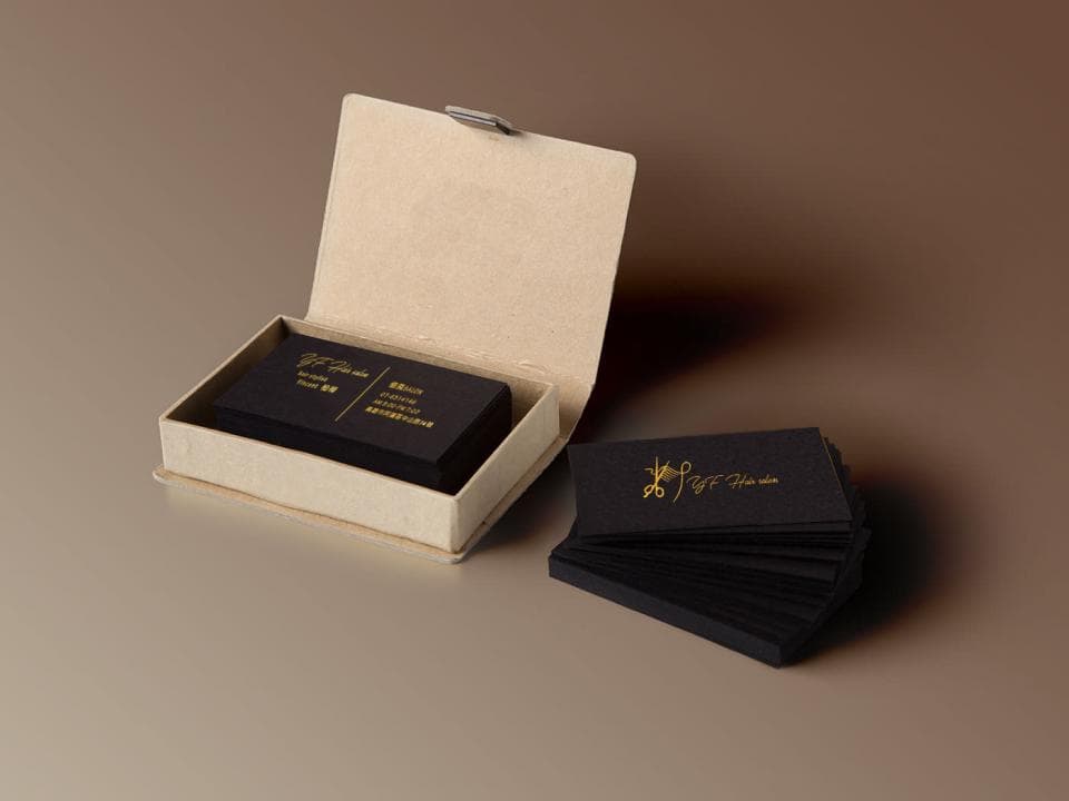 這張照片是金色的剪刀 logo 的名片,放在一個紙盒裡。