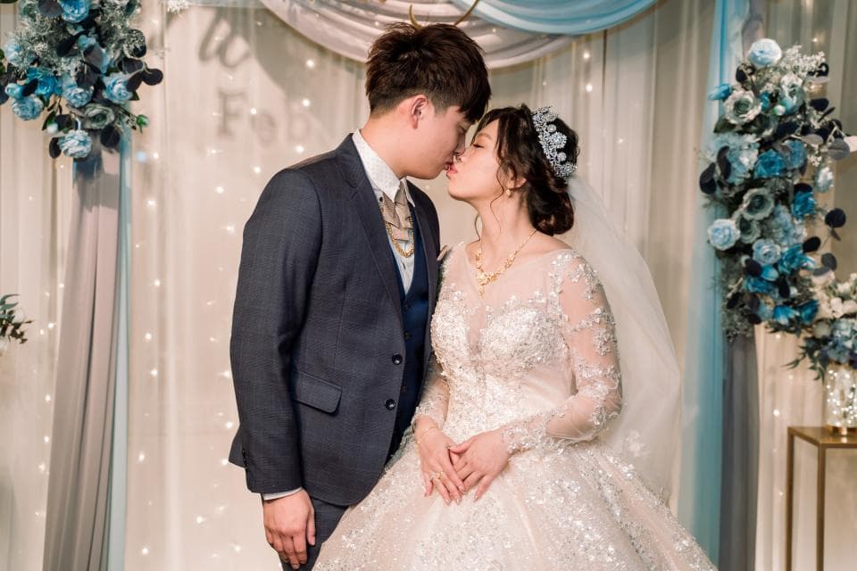 這張照片是一對新人正在深情擁吻,新郎穿著深色西裝,新娘穿著白色婚紗,他們互相依偎,彼此深情注視,畫面充滿了愛意和幸福。