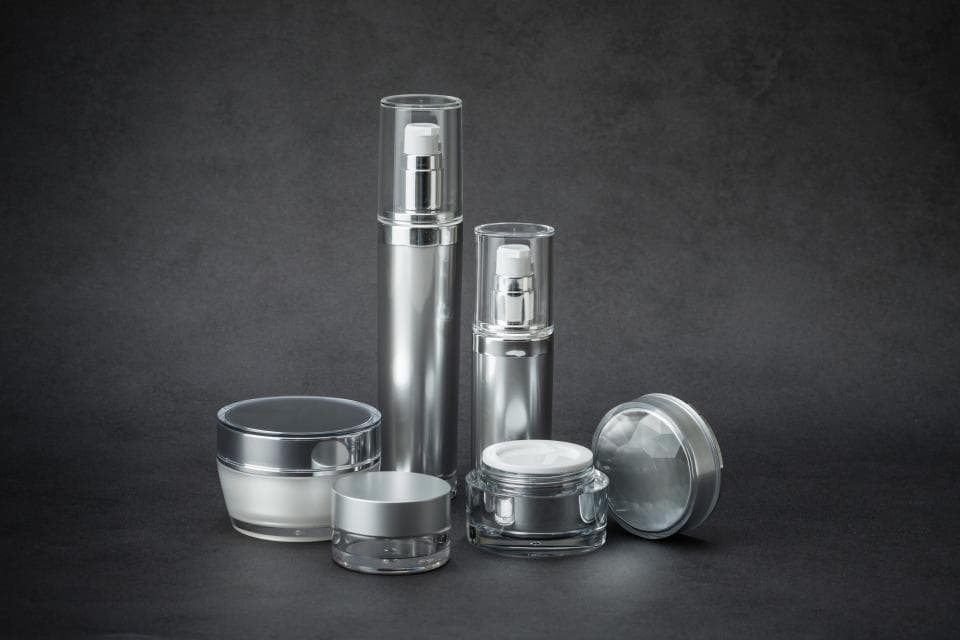 這張「護膚品」的照片是一組銀色瓶子和罐子,包括兩瓶精華液和兩個乳霜罐,擺放在黑色背景上。