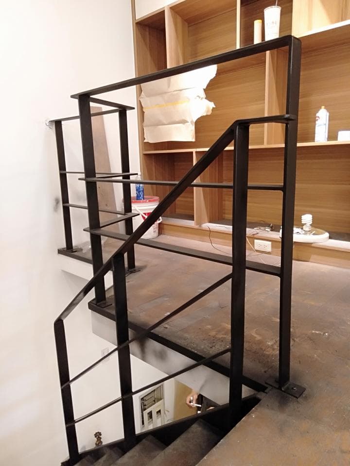 1) 這張照片顯示一個黑色金屬樓梯扶手,安裝在木架上,樓梯看起來是木質的,樓梯扶手的一部分也延伸到一個木架的前面