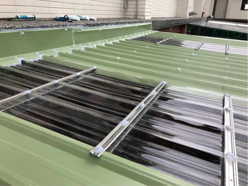 1) 照片顯示一個綠色的屋頂,上面安裝了透明的塑膠瓦,塑膠瓦的周圍有白色的密封膠