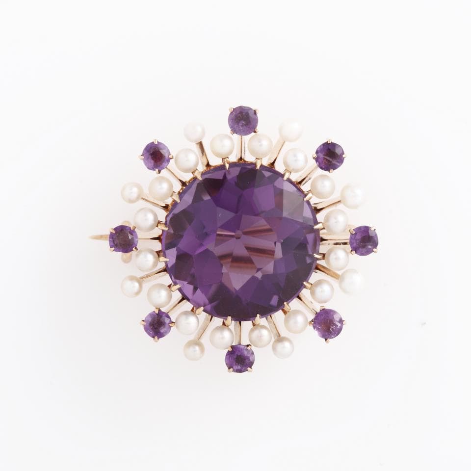 這張照片是一枚以紫水晶為中心的胸針,周圍環繞著一圈珍珠。紫水晶是中心的主石,閃耀著迷人的紫色光芒,珍珠則襯托出紫水晶的華麗,整個胸針看起來非常優雅。