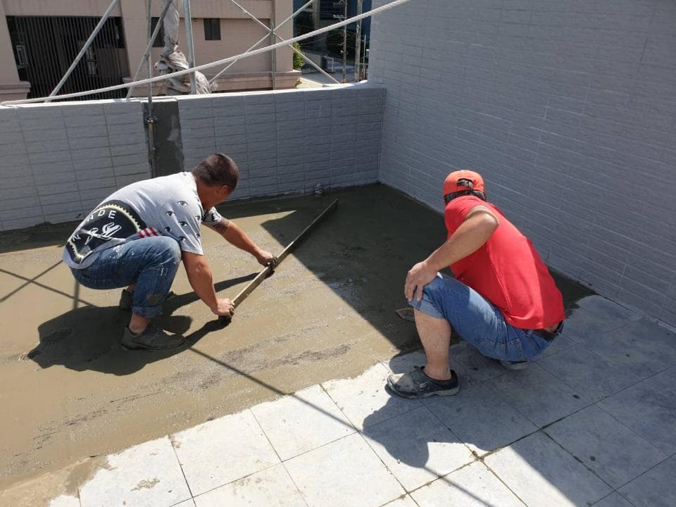 1) 照片顯示兩名男子正在一個水泥地面上工作,其中一人用木板工具平整地面