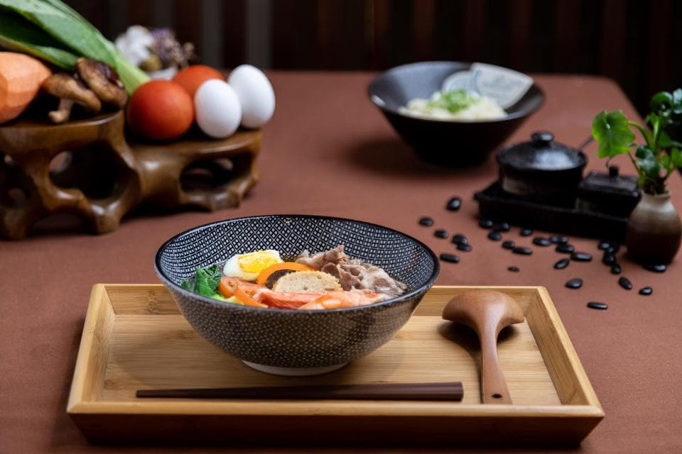 這張「一碗熱騰騰的日式拉麵」的照片是,擺放在木質餐盤上,周圍有筷子、湯匙和一些配菜。