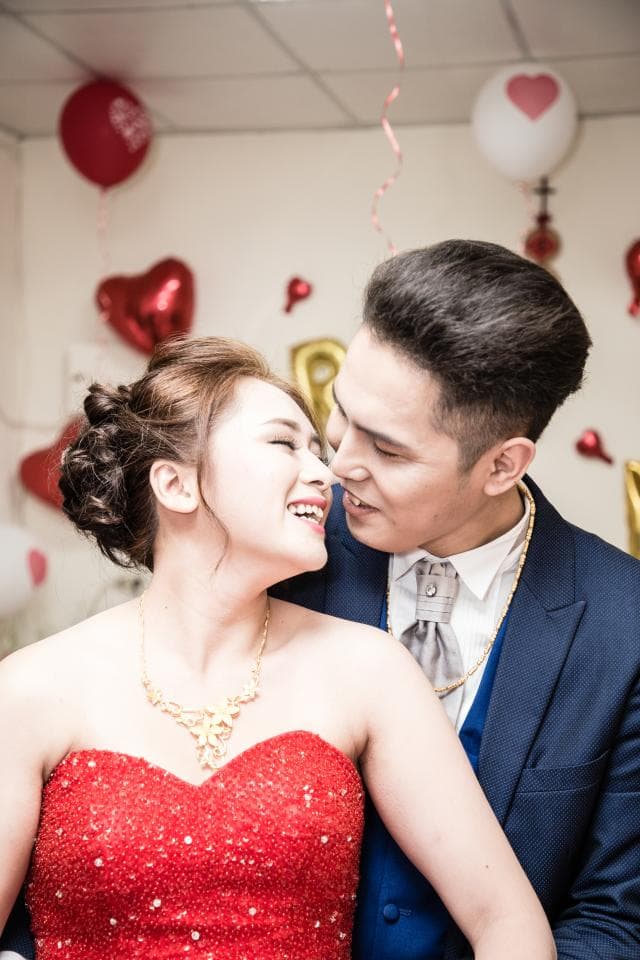 這張「婚禮」的照片是一對新人深情對望,新娘穿著紅色禮服,新郎穿著西裝,背景佈置有紅色氣球和愛心裝飾。