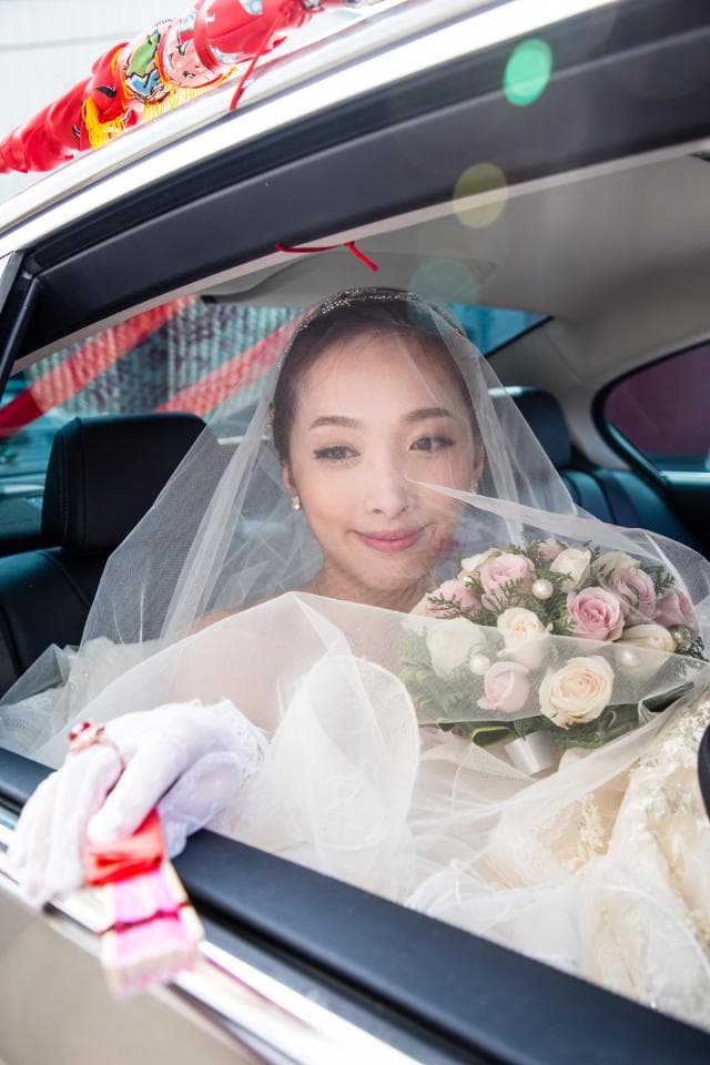這張照片是一輛婚禮車,裡面有一位穿著婚紗的新娘,她頭戴白紗,手持捧花,露出幸福的笑容,看起來非常美麗。