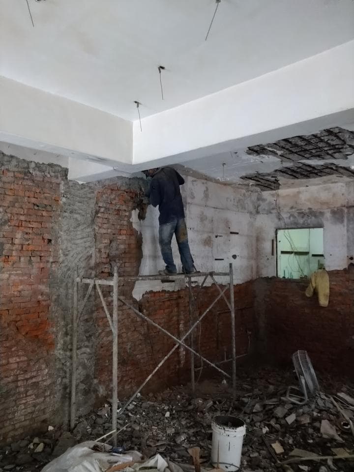 1) 照片顯示一個工人在一個正在進行裝修的房間內工作,他站在一個搭建好的鷹架上,房間牆壁的部分已經被拆除,露出了裡面的磚塊