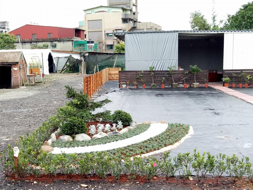 這張照片是一個花園,裡面有一個小型的圓形花壇,裡面種植了一些花卉植物,以及一些裝飾性的石頭。花壇周圍圍繞著一些矮灌木和綠色的草坪。