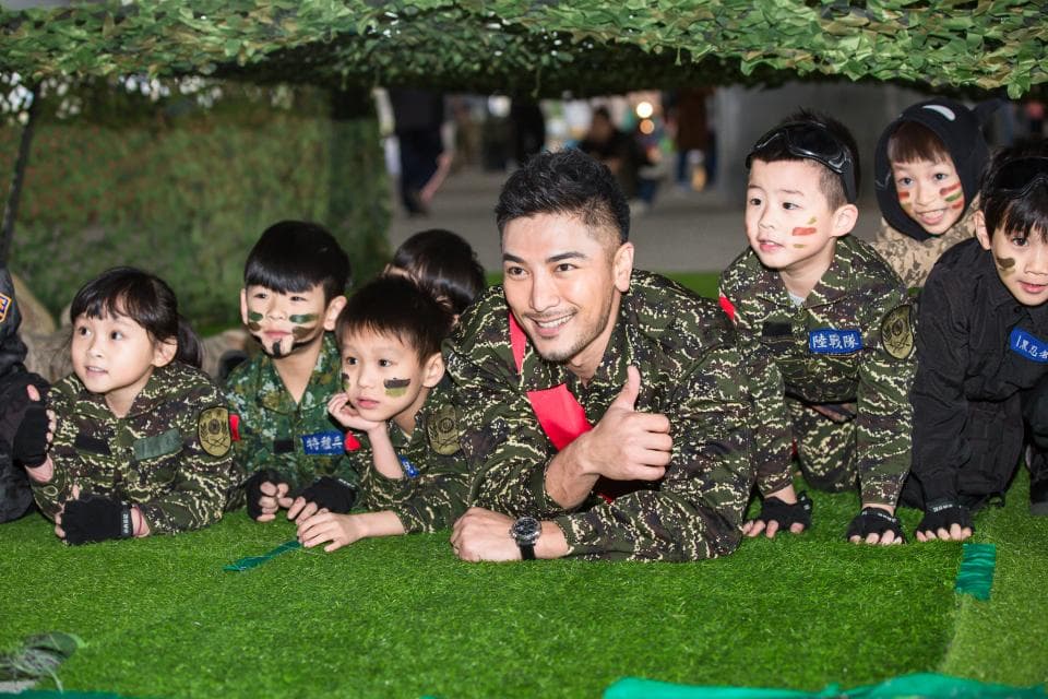 這張照片是幾位小朋友和一位成年男性在草地上玩耍,他們都穿著迷彩服,看起來很開心。