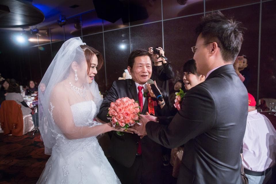 這張照片是一對新人正在交換戒指,新娘穿著白色婚紗,新郎穿著黑色西裝,他們都非常開心。