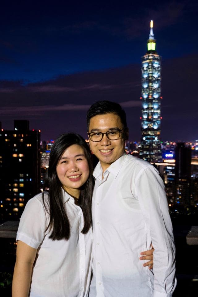這張照片是一對情侶在臺北101大樓前合影,他們身穿白色襯衫,面帶微笑,展現出甜蜜幸福的模樣。