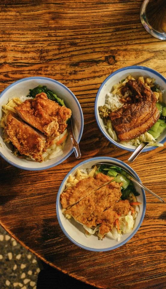 這張「三碗飯」的照片是一張木桌上的三碗飯,其中兩碗是炸雞,一碗是滷肉,都是臺灣常見的料理。