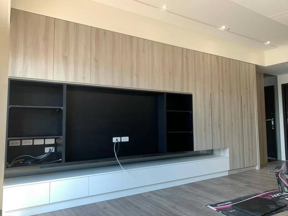 這張照片是一個現代化的客廳,最顯眼的是牆上的大型電視櫃,它由木板製成,並配有白色的抽屜,可以存放影音設備和其他物品。