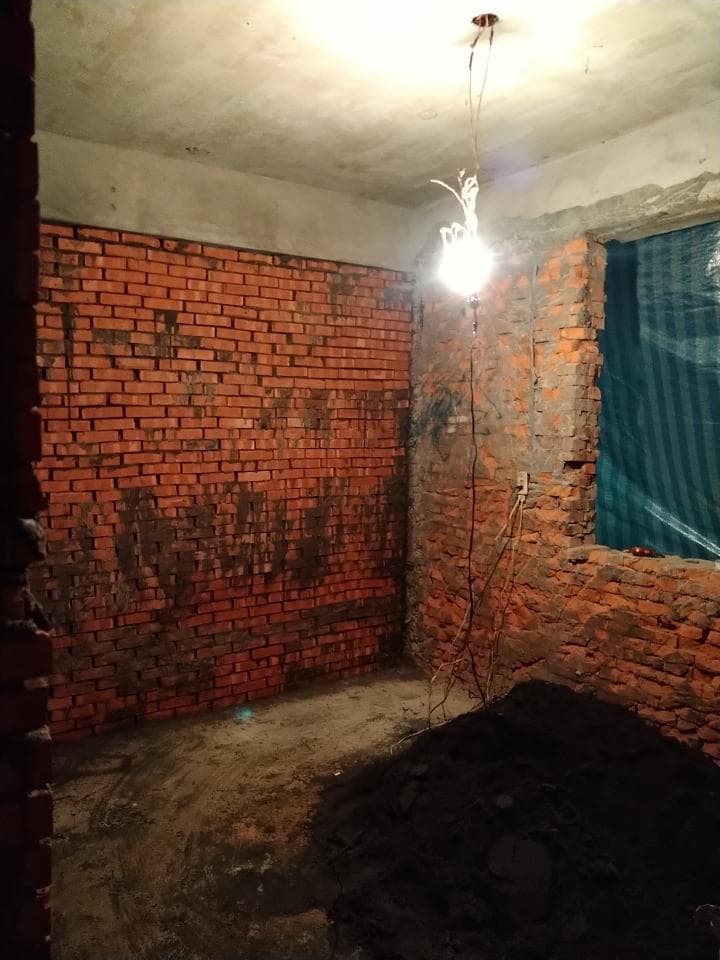 1) 照片顯示一個空房間,房間的牆壁是用紅磚砌成,天花板是水泥,房間中間有一堆黑色的泥土,房間的角落有一盞燈