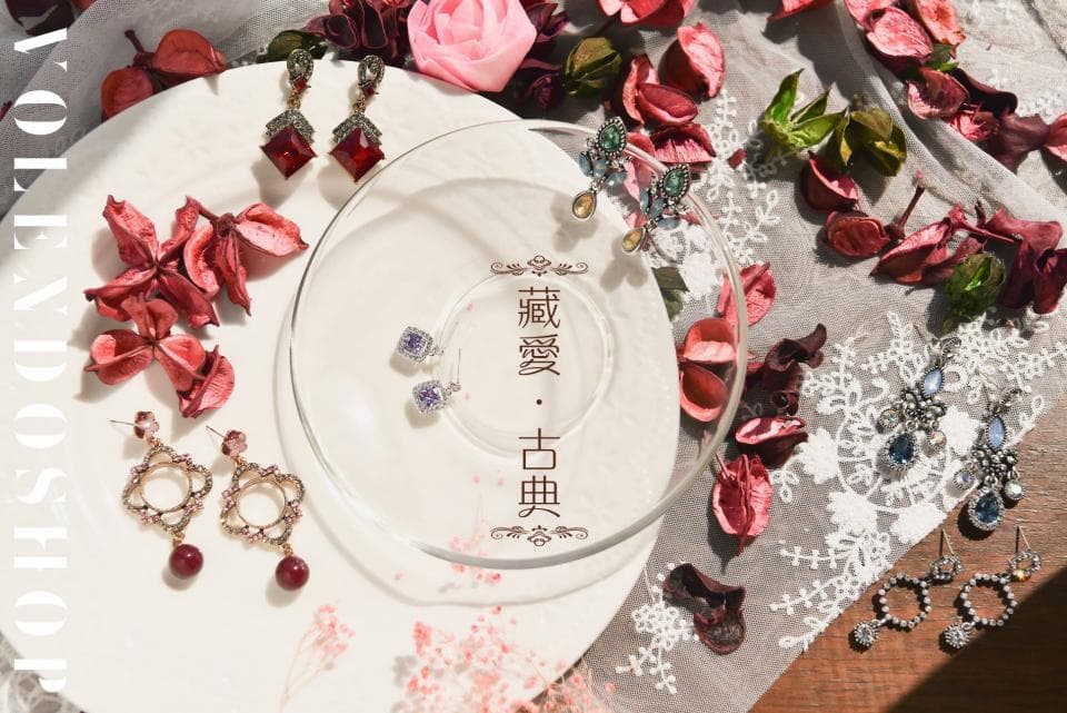 這張「耳環」的照片是各種款式和顏色的耳環,擺放在白色背景上,配有花朵和裝飾品。