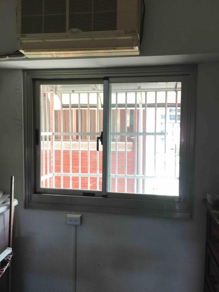 這張照片是一扇帶有鐵欄杆的窗戶,窗外有紅磚牆和綠色的植物。