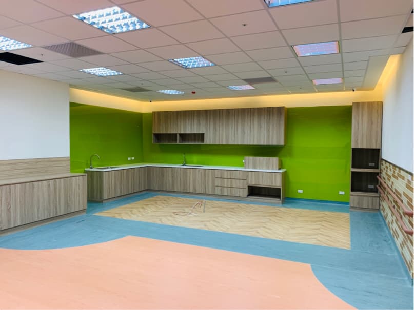 這張「廚房」的照片是一個現代化的廚房,有著木質的櫥櫃和綠色的牆壁。地板鋪著木紋地磚,中間有一塊藍色的地磚,整體設計簡潔明亮。