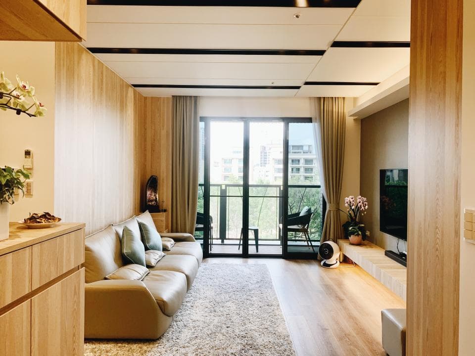 這張「客廳」的照片是一個以木質元素為主,並帶有簡約風格的空間。房間中央放著一張沙發,旁邊有一臺電視和一個落地扇。牆上裝飾著一些綠色植物,整體看起來非常舒適溫馨。