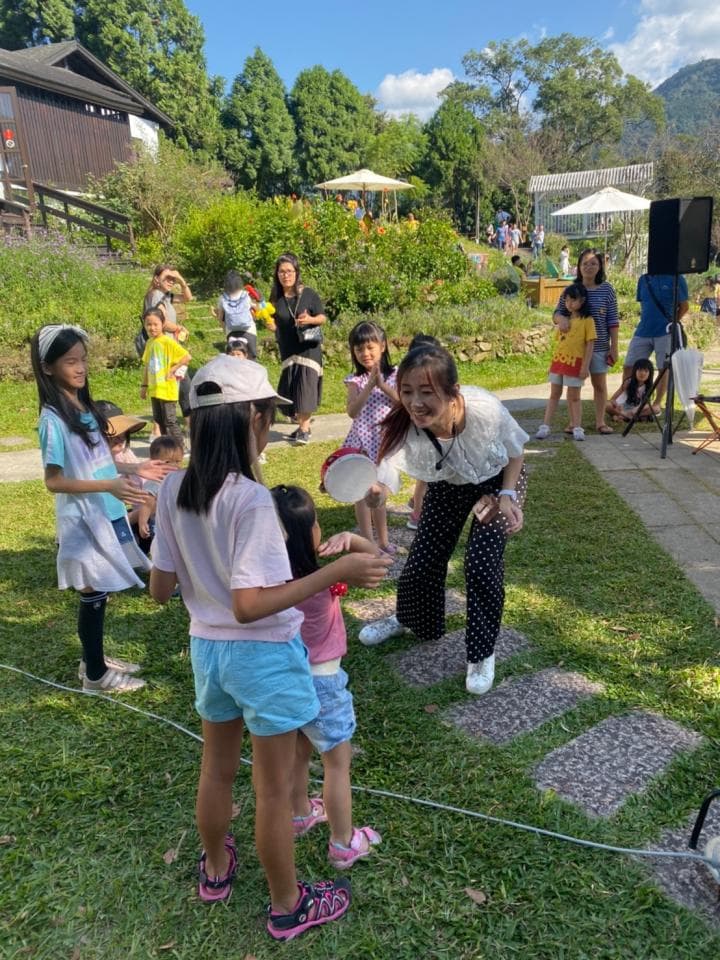 這張照片是一個戶外遊戲場景,一群小朋友和大人在玩遊戲,中間一個女孩正用手拿著一個白色盤子,看起來很開心。