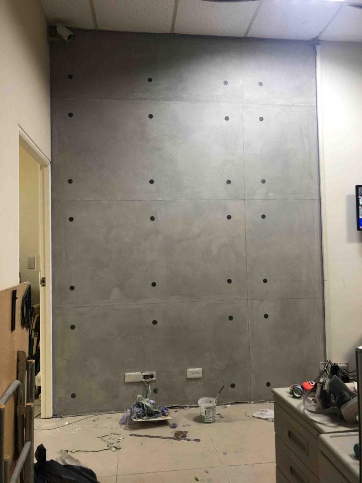 1) 照片顯示一間房間內的一面牆壁,牆面是水泥材質,表面有許多小圓孔