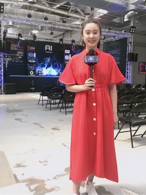 這張照片是一個年輕女子站在一個舞臺前面,她穿著一件紅色的連衣裙,手裡拿著一個麥克風,正在微笑。