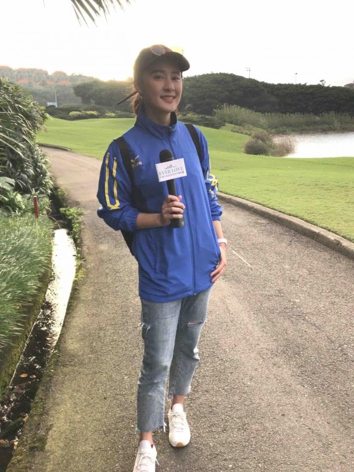 這張「高爾夫球場」的照片是一位穿著藍色外套和牛仔褲的女子,她拿著麥克風站在綠色草地上。