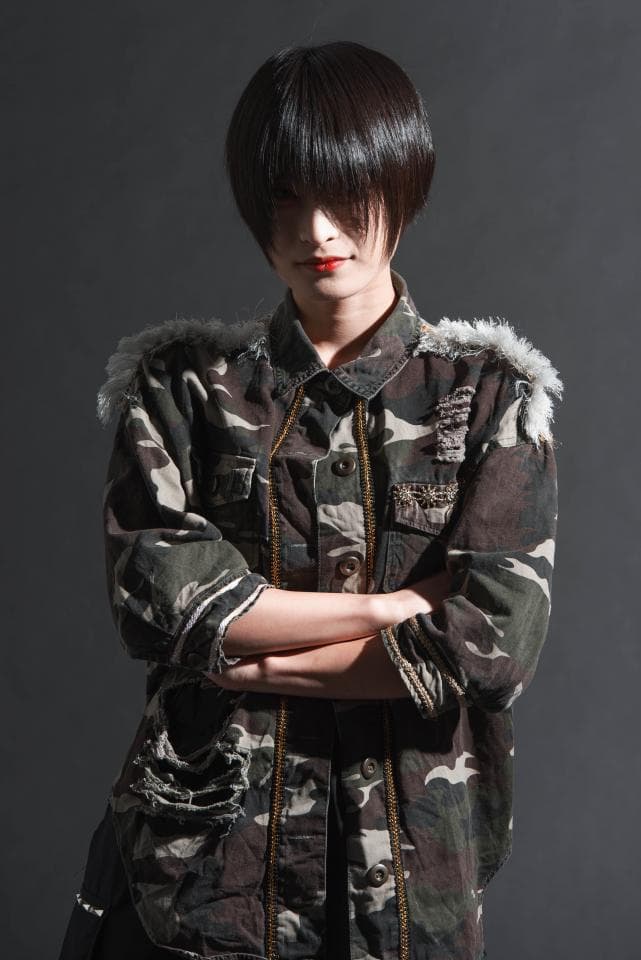 這張「時尚街拍」的照片是一個戴著墨鏡的短髮女孩,她穿著一件迷彩外套,雙手交叉,展現出冷酷的眼神和個性。