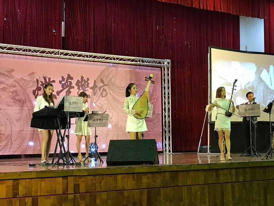 這張照片是四個年輕女子在舞臺上表演音樂。她們穿著白色的衣服,並演奏各種樂器,包括琵琶和二胡。舞臺上還有音響設備,讓她們的音樂傳播到觀眾席。