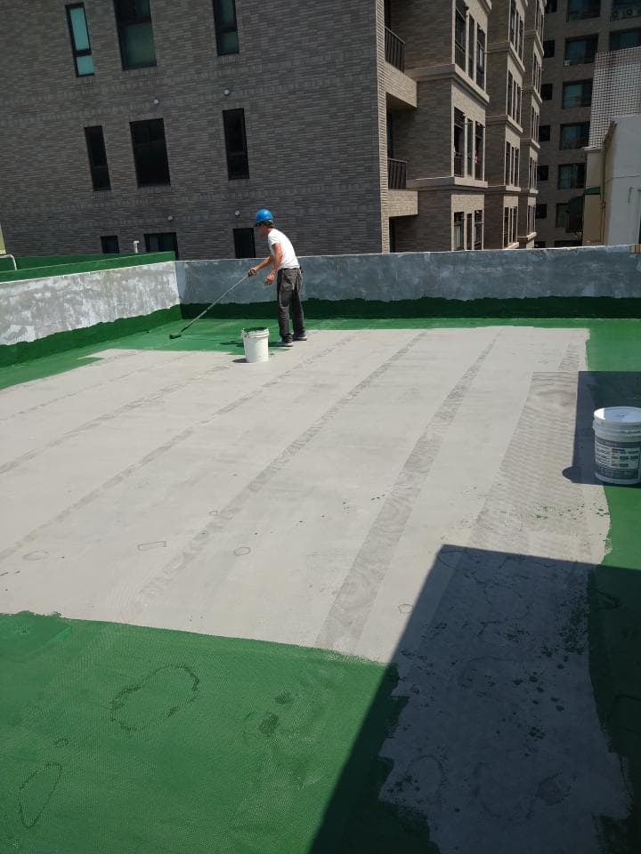 1) 照片顯示一位身穿藍色安全帽的工人正在建築物頂樓的防水層上塗抹水泥