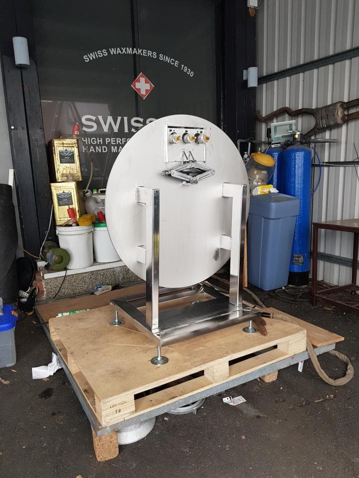 1) 照片顯示一個銀色的圓形物體,放在木質平台上,平台下方有四個螺絲,平台周圍有幾個木板