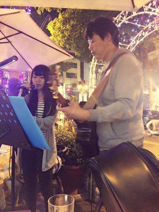 這張「一個女孩和一個男孩在街頭演奏」的照片是,女孩穿著條紋上衣,手持麥克風唱歌;男孩穿著灰色的連帽外套,彈著吉他。