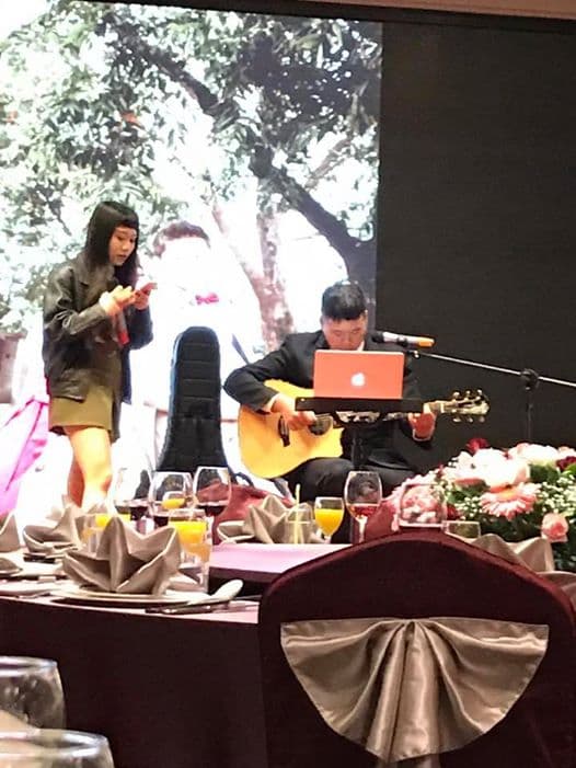 這張「婚禮」的照片是,一個女生站在臺上唱歌,而一個男生在臺下彈吉他,舞臺上還放著一個筆記型電腦。