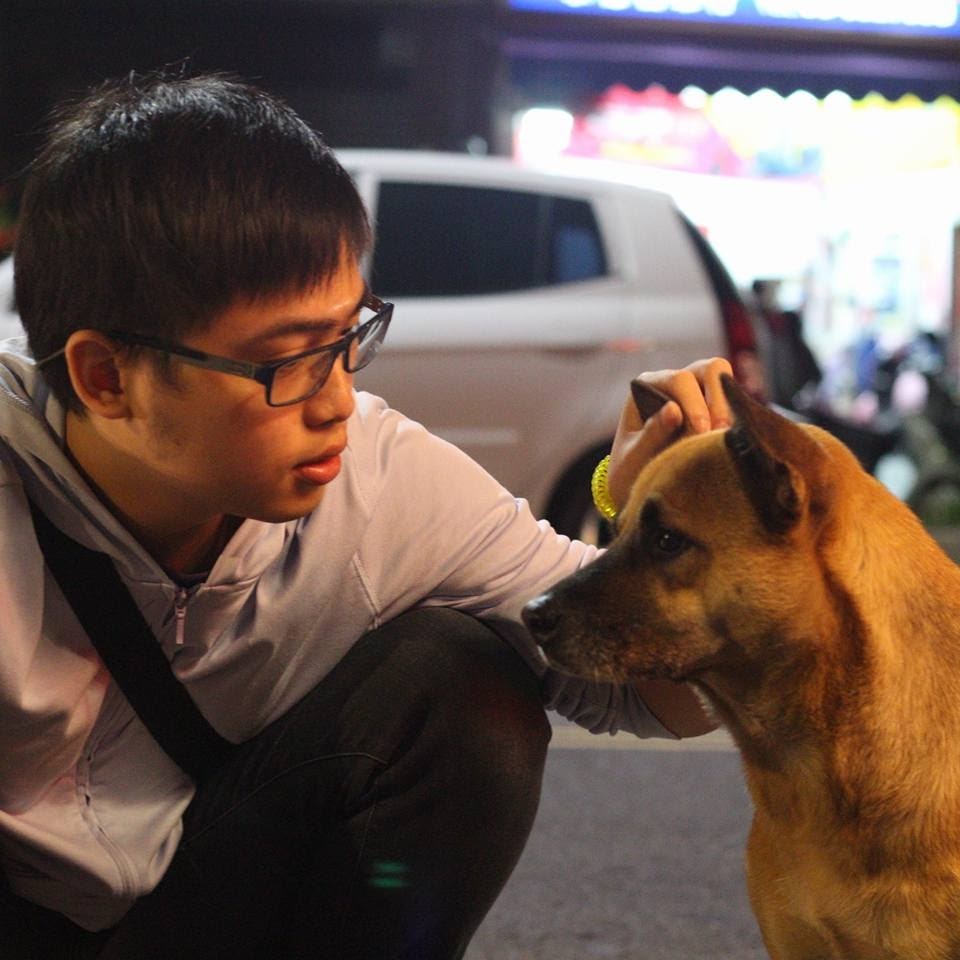 這張照片是 一個年輕人正在撫摸一隻狗的頭部。他的手輕輕放在狗的頭上,狗狗看起來很享受這個動作,閉著眼睛露出放鬆的表情。