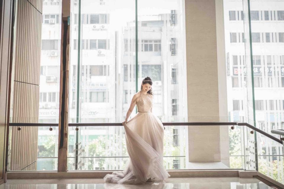 這張「婚紗照」的照片是一個穿著白色婚紗的女子,站在落地窗前,背景是城市景觀,她正在整理自己的婚紗。