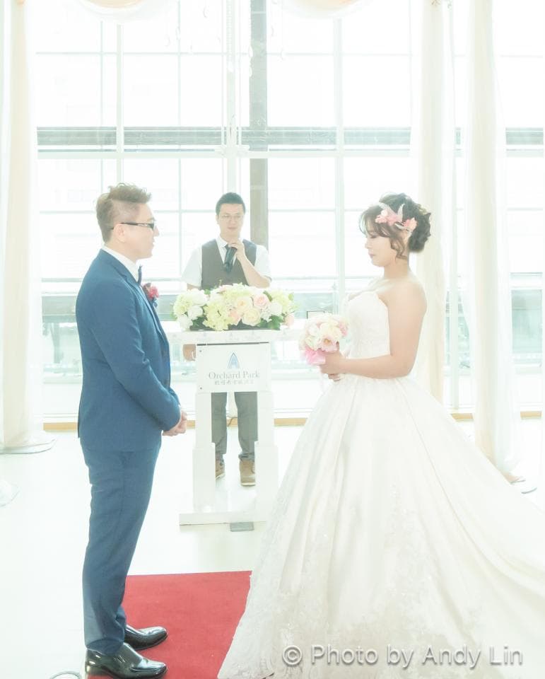 這張「婚禮」的照片是一個穿著白紗的新娘和新郎,他們站在一個白色的平臺上。 新娘手拿著花束,而新郎則穿著藍色的西裝。