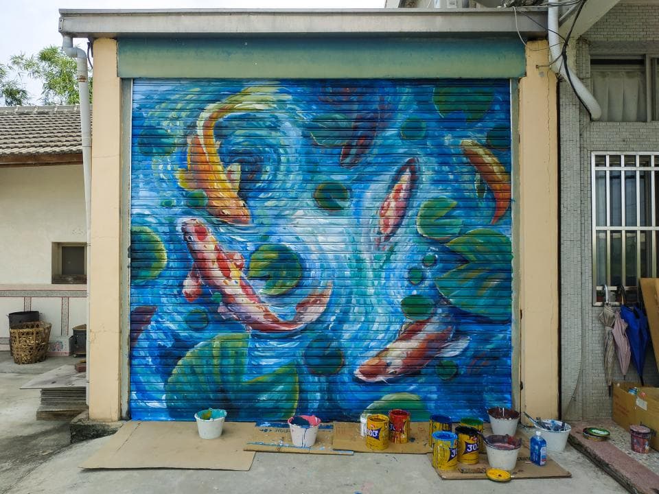 這張「牆上繪畫」的照片是一幅描繪著水中游動的金魚的藝術作品,背景是藍色的水波,並以綠色植物點綴。