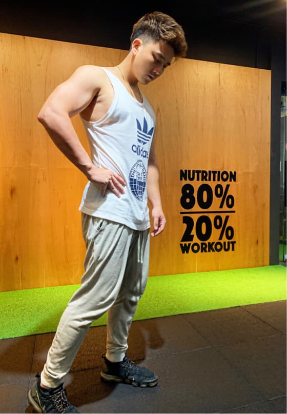 這張「健身房」的照片是一位穿著白色背心和灰色運動褲的男子,背景是木頭牆壁和綠色地毯,牆上寫著「營養80%,運動20%」。