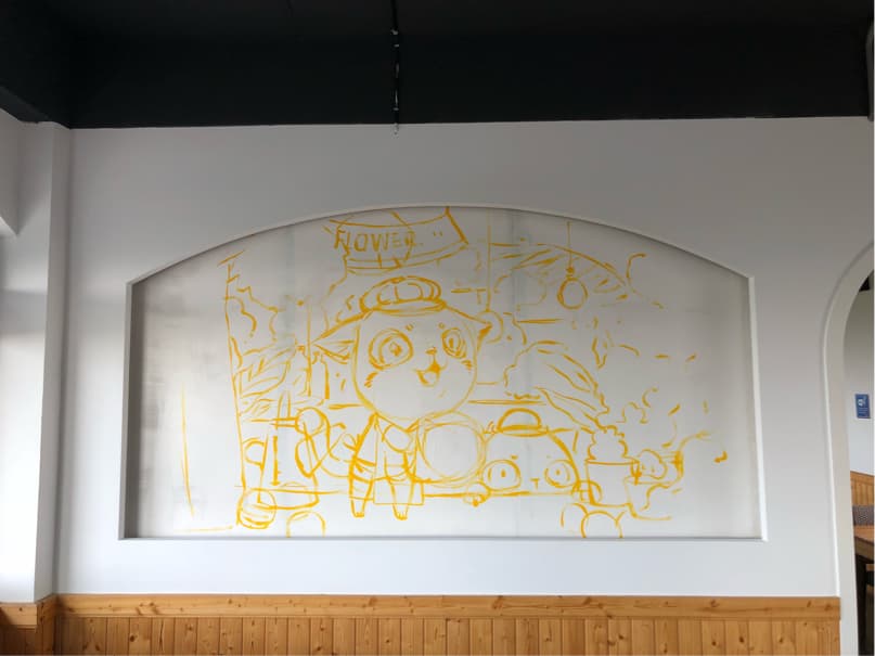 這張「牆壁」的照片是一個用黃色畫筆繪製的圖案,描繪了卡通人物,以及一些植物和文字。