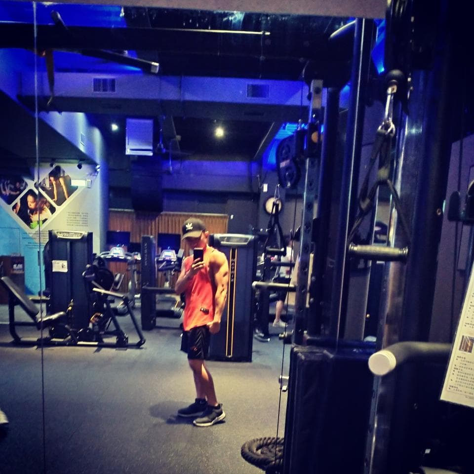 這張照片是一個男人在健身房裡,他戴著帽子,穿著紅色的上衣,在使用健身器材。他看起來很專注,正在鍛鍊身體。