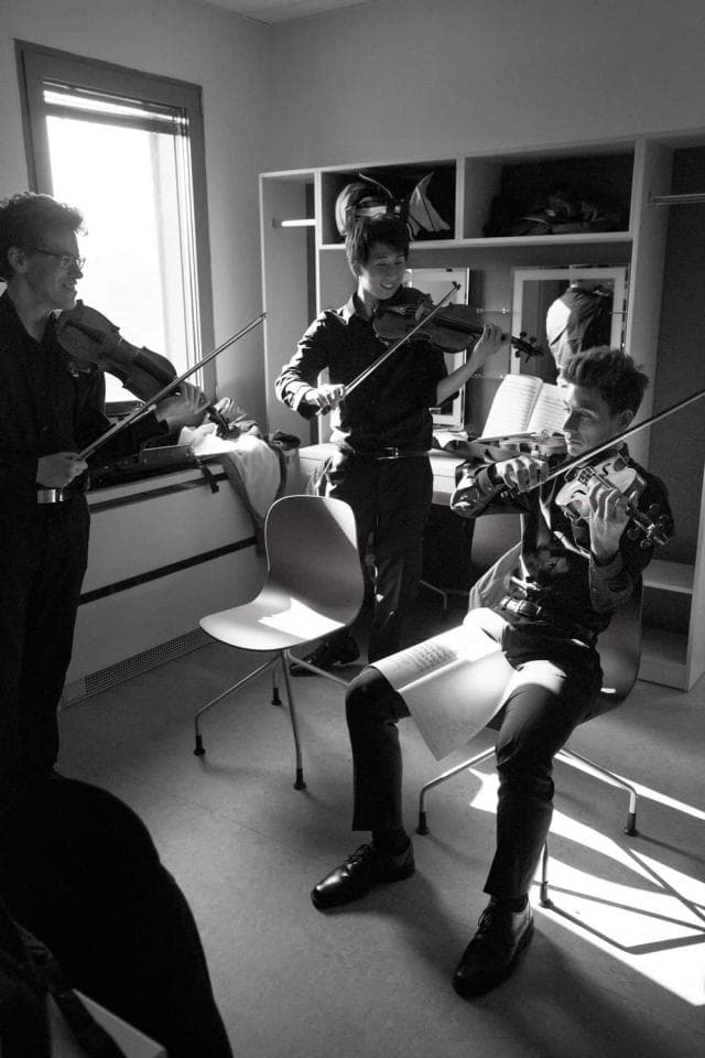 1) 照片中顯示有三位穿著黑色衣服的年輕人在一個房間裡,其中兩個人拿著小提琴,另一個人則演奏著小提琴